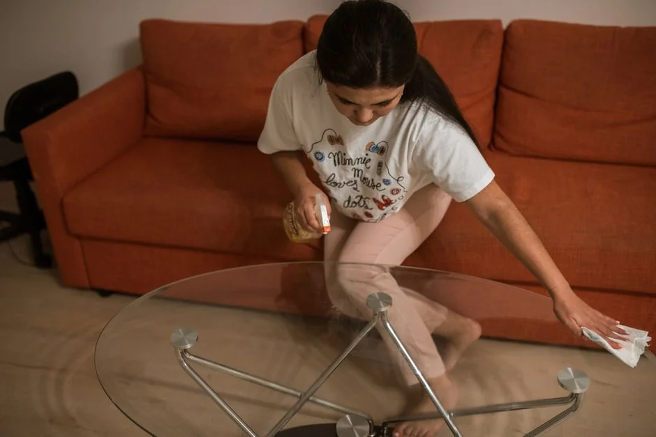 A woman in a gray sweater carefully wipes a table, highlighting comfortable home cleaning.